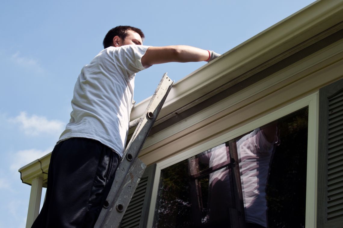 Man standing on ladder and decluttering house roof
