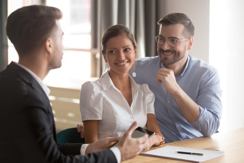 Happy millennial couple listening to male financial business advisor, lawyer or banker. Broker, insurance manager or real estate agent proposes good new deal to young smiling family at office meeting