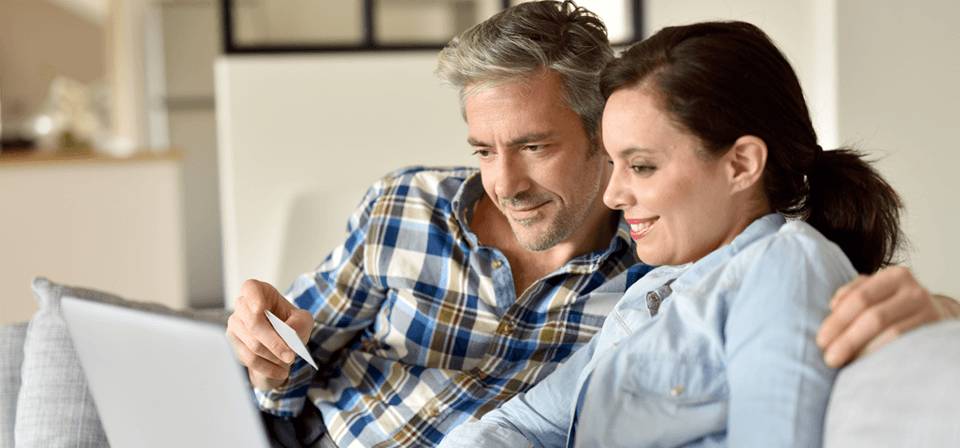 Man and woman couple staring at computer screen with man holding card